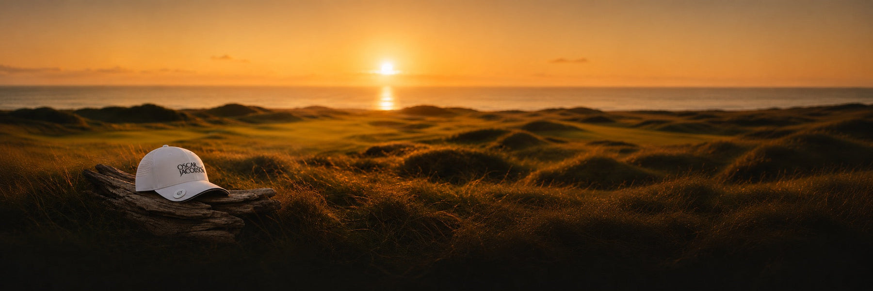 Golden-hour links coastline with an Oscar Jacobson cap, evoking the brand's Swedish heritage