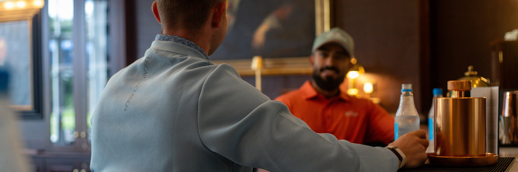 Two golfers in smart Oscar Jacobson polos and layers at a clubhouse, dressed within a typical golf dress code