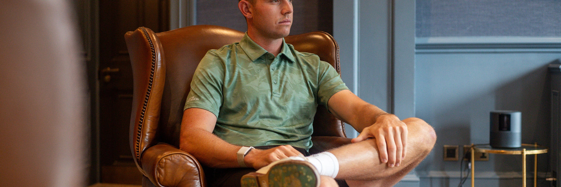 A golfer in an Oscar Jacobson polo, seated in a clubhouse leather armchair