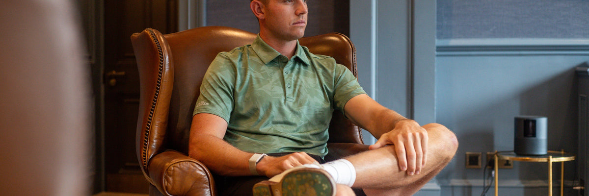 A golfer in an Oscar Jacobson polo, seated in a clubhouse leather armchair