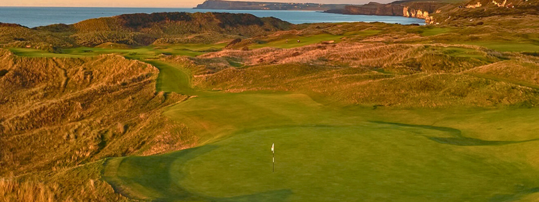 A links course at golden hour, dunes and firm fairway running down to the sea